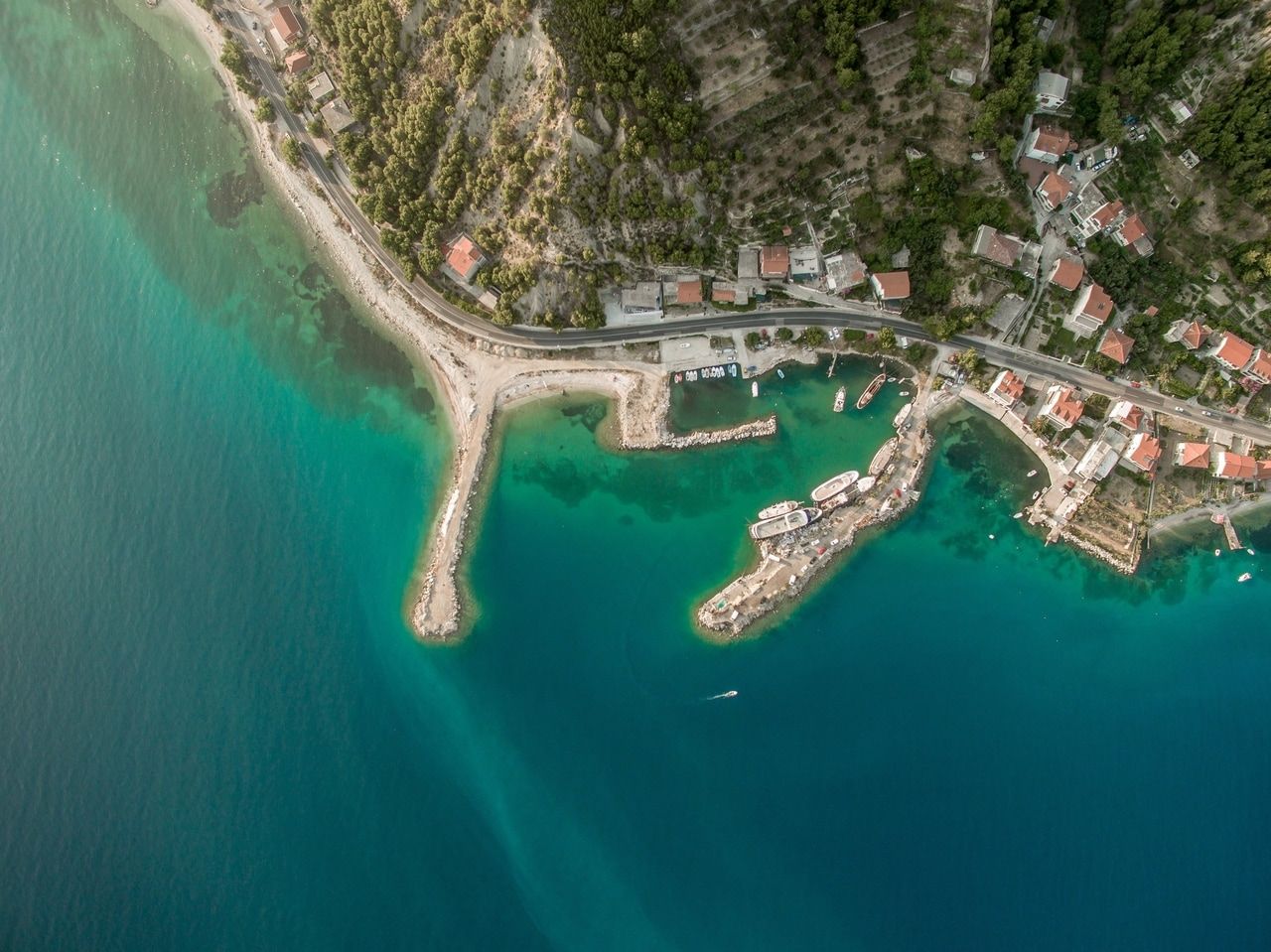 Въздушна снимка на крайбрежно село с тюркоазени води и лодки близо до брега.