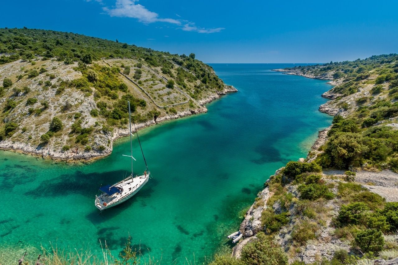 Bucht mit türkisfarbenem Wasser und einer Segelyacht, umgeben von grünen Hügeln.