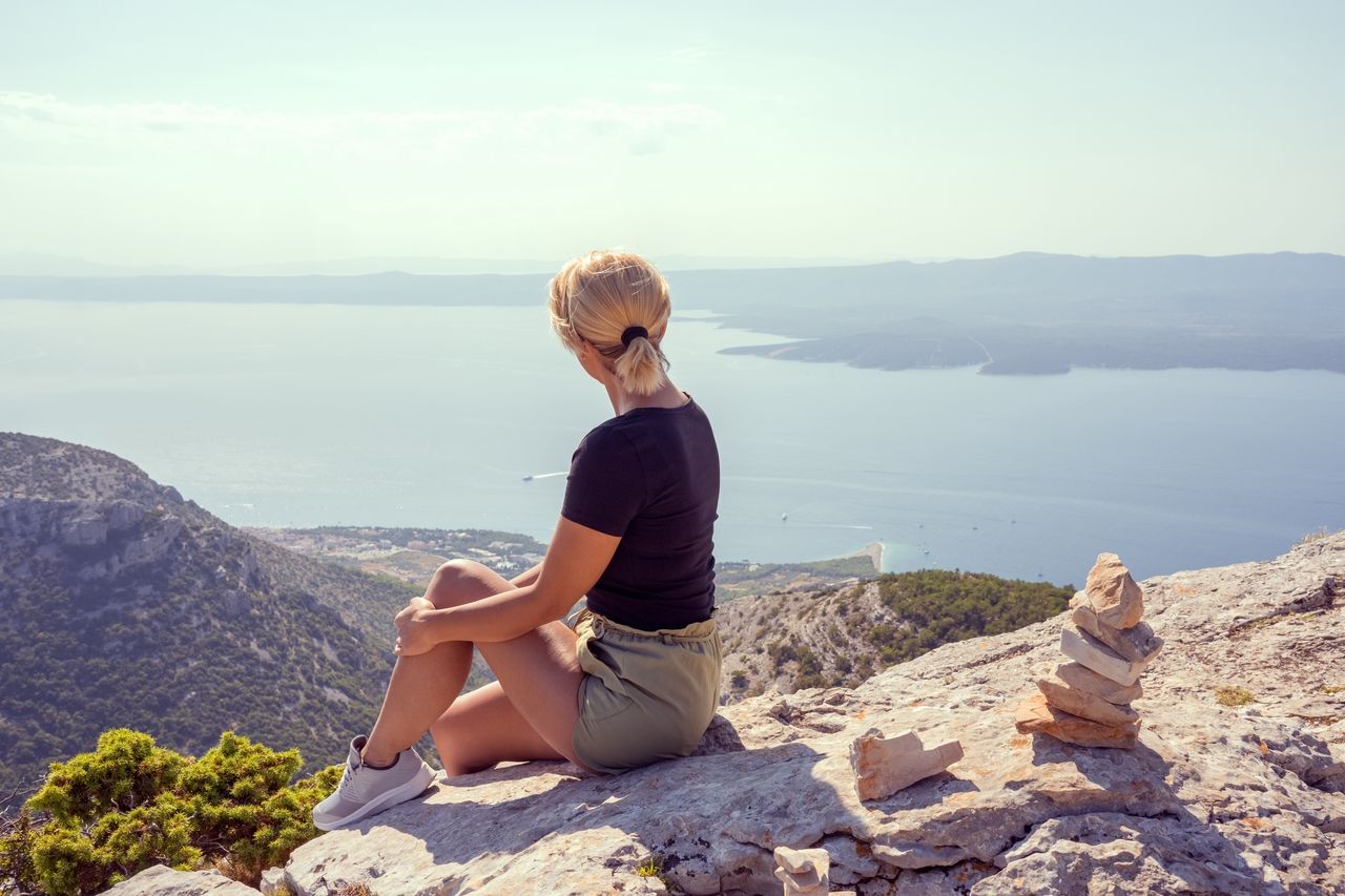 Egy nő ül egy sziklán a Vidova Gora csúcsán, Brač szigetén, és élvezi a kilátást a tengerre és a környező szigetekre.