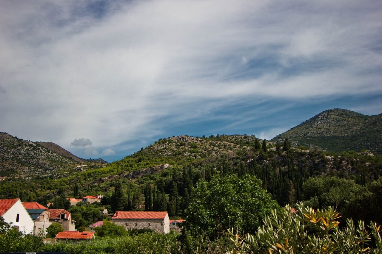 Picturesque village in Croatia, nestled in a hilly landscape with lush vegetation and traditional houses with red roofs. The clear sky and green hills create a peaceful and idyllic atmosphere.