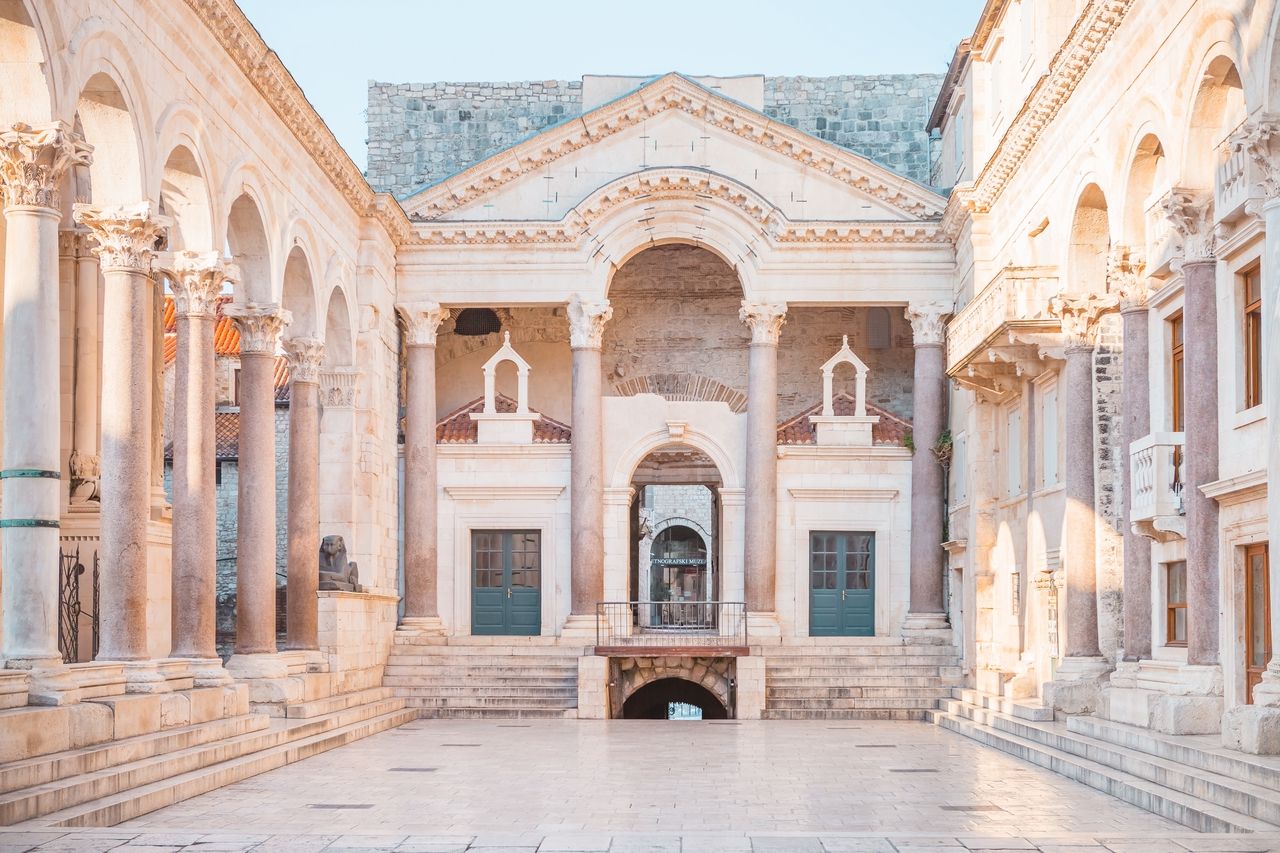 Eine Ansicht des Peristyls im Diokletianpalast in Split, Kroatien. Die beeindruckende römische Architektur mit hohen Säulen und eleganten Bögen ist in weichem Morgenlicht beleuchtet.