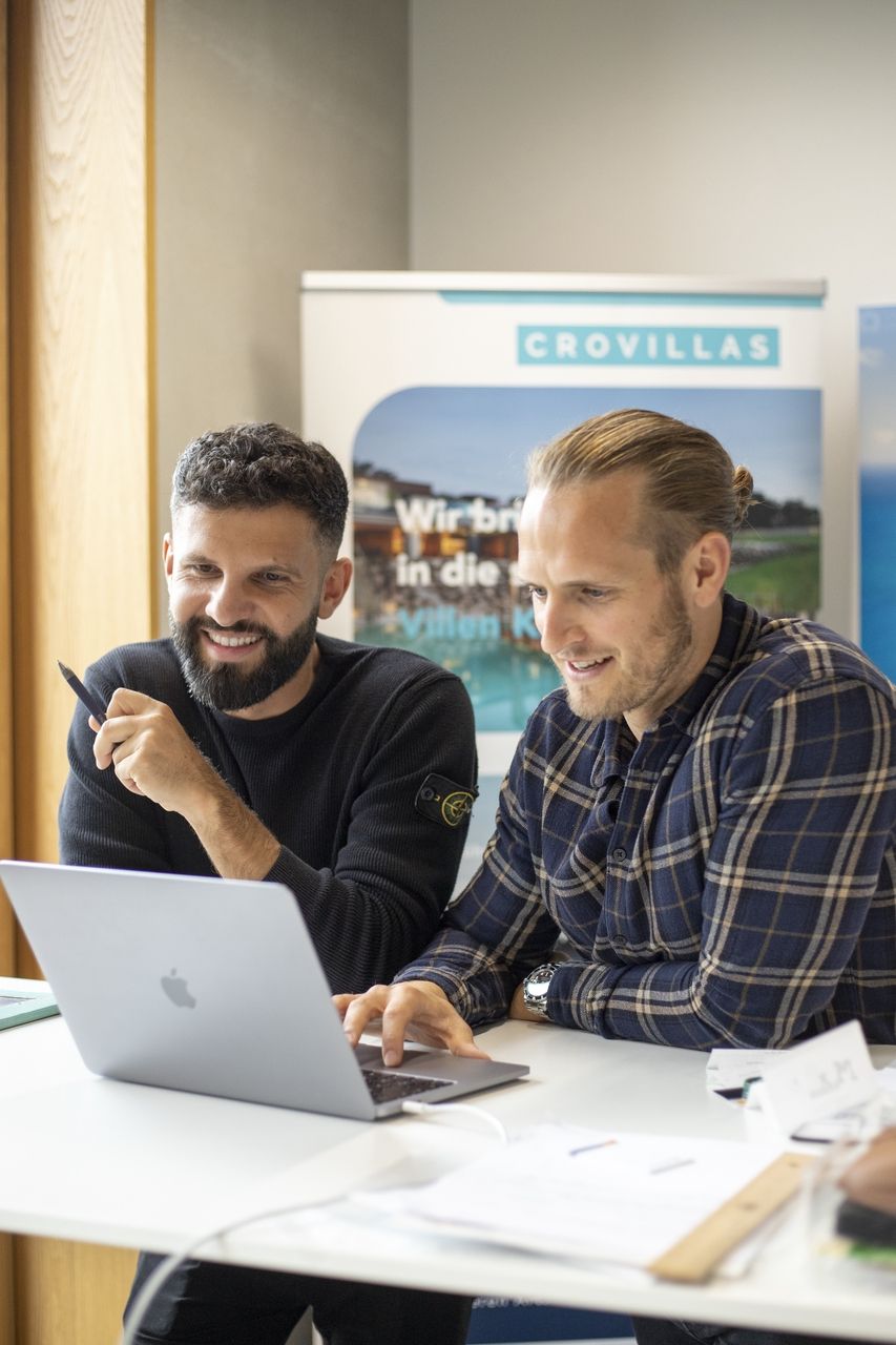 Valentino und Dogan sitzen an einem Tisch und arbeiten an einem Laptop.