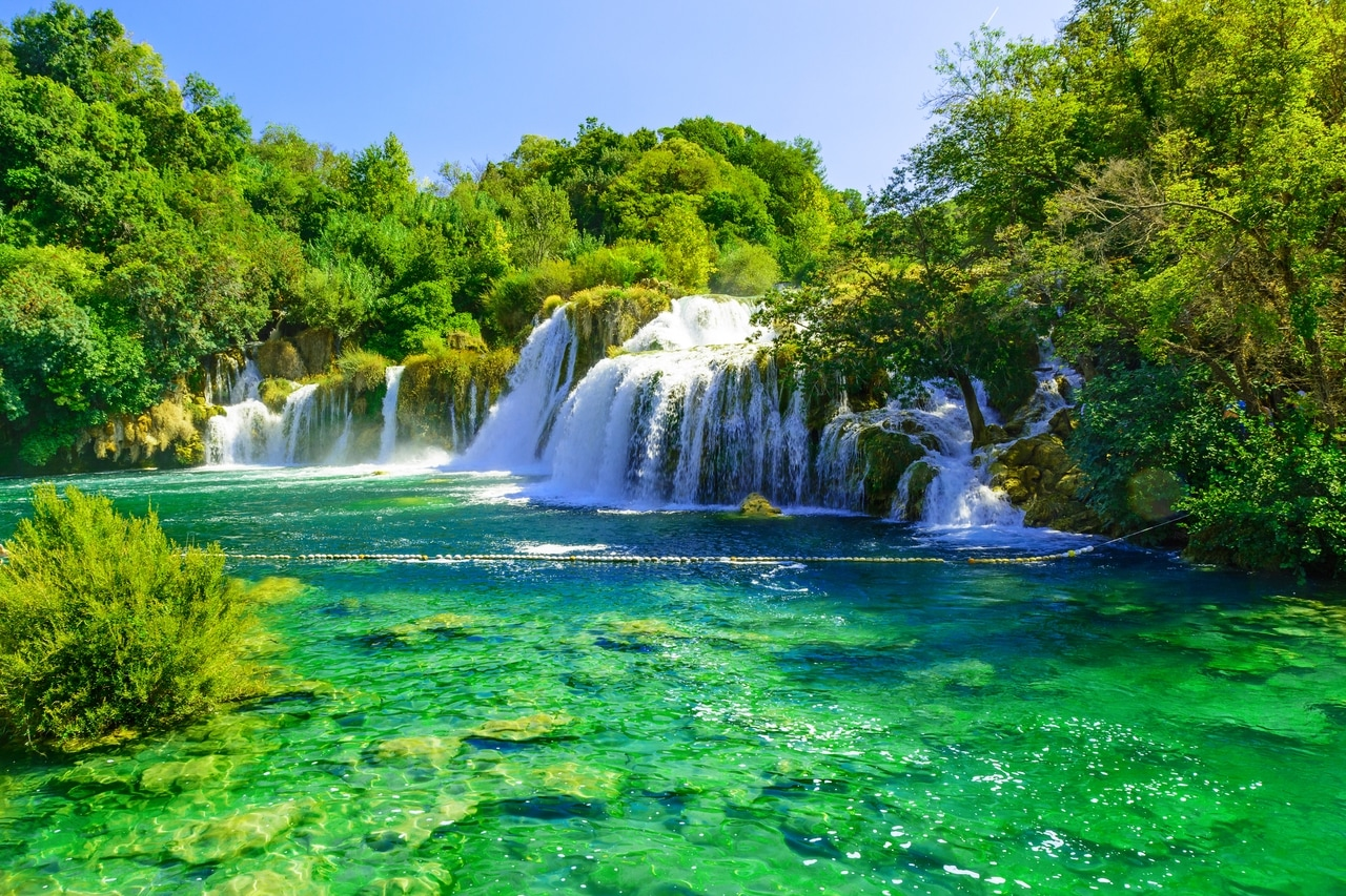 Spectacular waterfalls in Krka National Park in Croatia, surrounded by lush green vegetation and crystal-clear, emerald-green water. The natural beauty of the park offers a picturesque and refreshing nature experience.