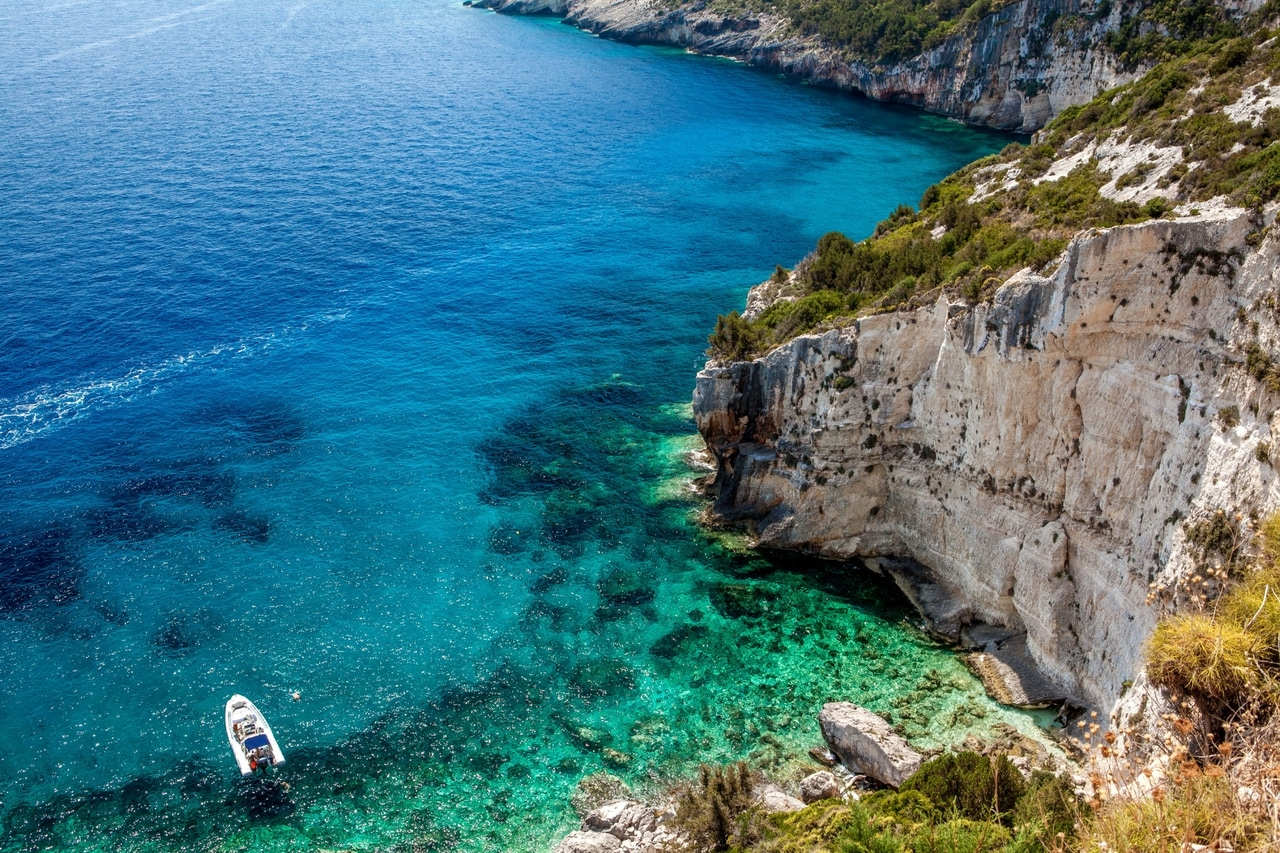 Häpnadsväckande utsikt över en klippig kust i Kroatien med kristallklart, turkosfärgat vatten. En liten båt ligger för ankar i viken, omgiven av frodig vegetation och branta klippor som framhäver Adriatiska havets naturliga skönhet.