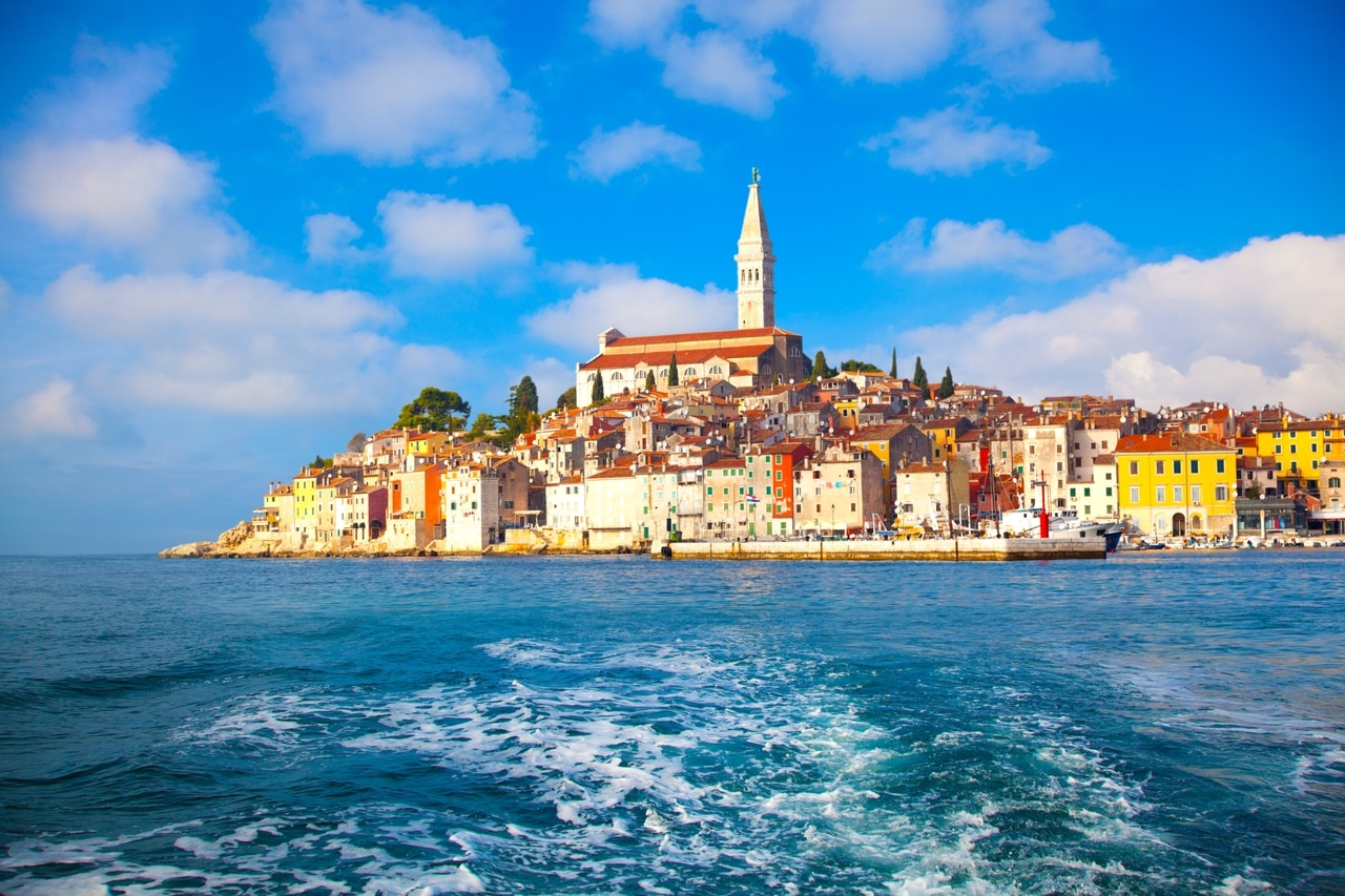 Panoramic view of the coastal town of Rovinj in Istria, Croatia, with its colorful buildings and the distinctive Church of St. Euphemia. The town is picturesquely situated on the Adriatic coast under a bright blue sky.