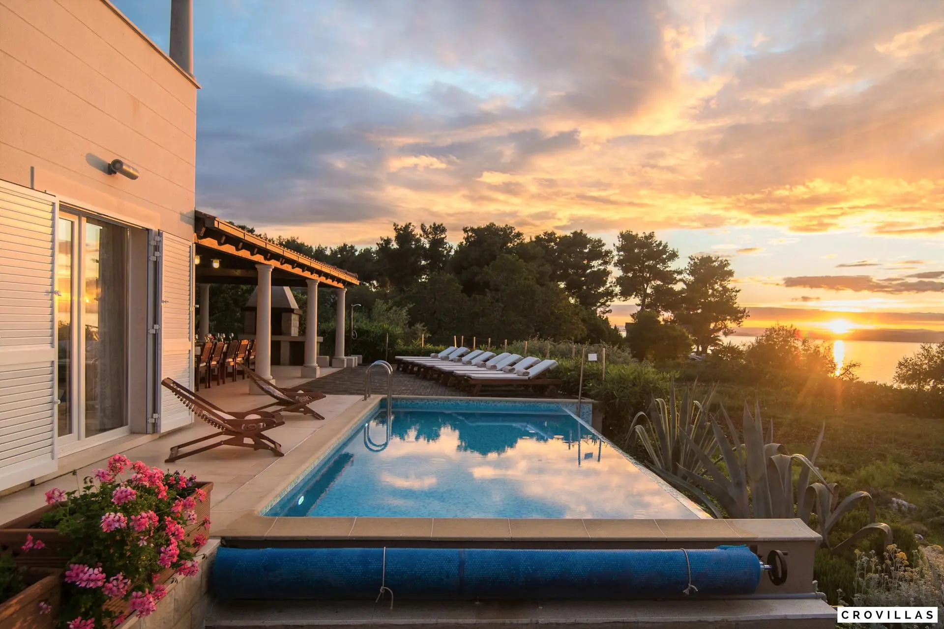 Luxe villa op het eiland Brac met zwembad en uitzicht op zee bij zonsondergang, omgeven door groene vegetatie en bloeiende planten. Het terras biedt ligstoelen en een eetgedeelte buiten, ideaal voor ontspannen avonden.